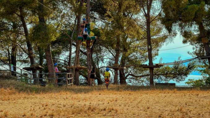 Outdoor adventure park with people navigating tree obstacles in Liguria, Italy.